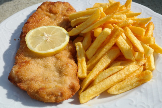 Paniertes Schnitzel mit Pommes und Zitronenscheibe auf einem Teller